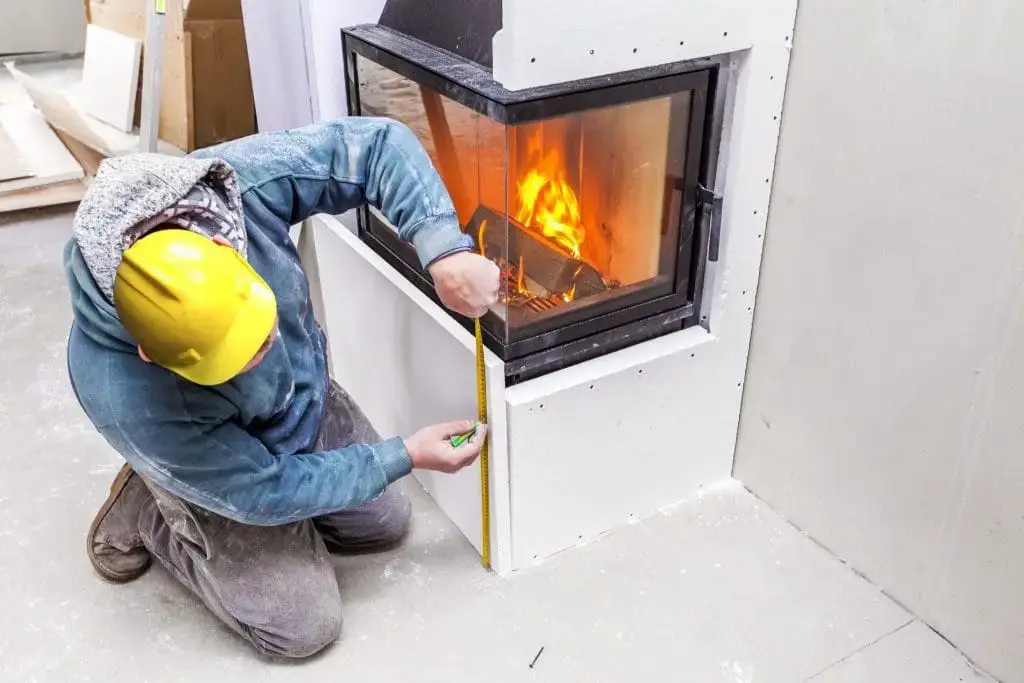 Contractor measuring fireplace installation during winter renovation project.
