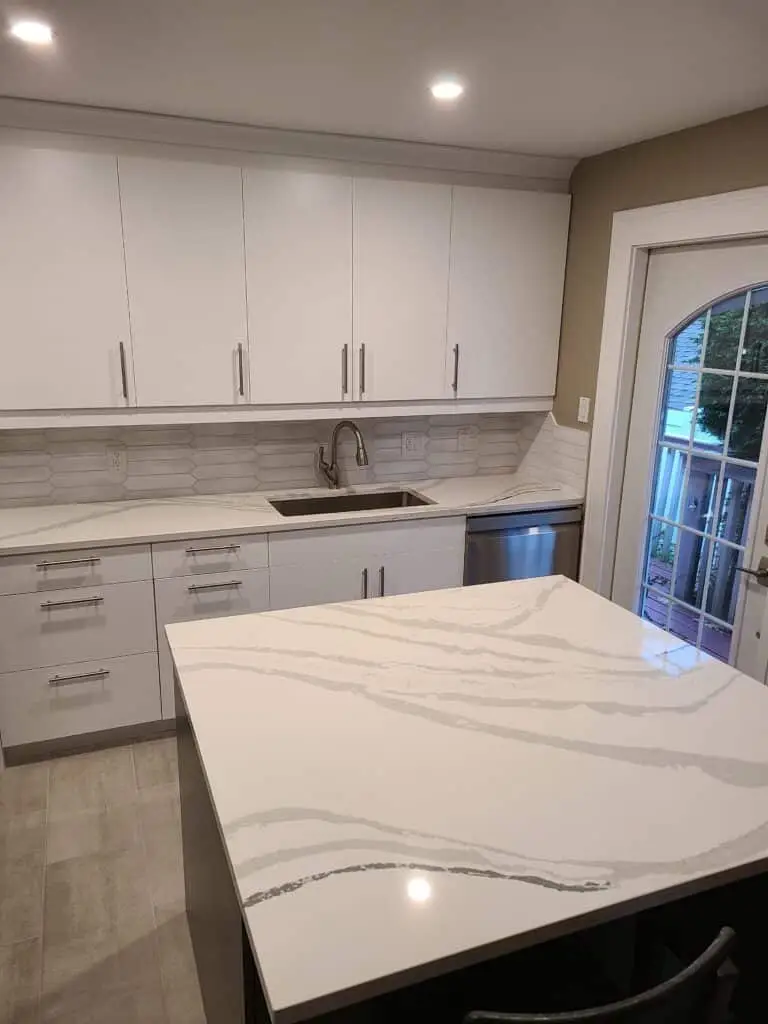 Modern white kitchen cabinetry and countertops with quartz detailing and stainless steel sink.
